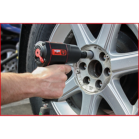 Ein Mann hält einen schwarzen und roten Schlagschrauber an einem silbernen Rad. Der Schrauber wird gerade zum Lösen der Radmutter verwendet.